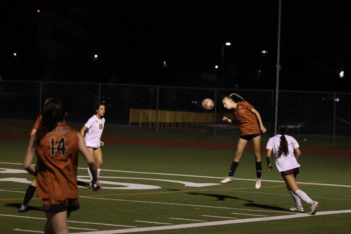 Jumping into the air, Tayla Score '25 heads the ball towards the goal. A few moments later, the Warriors gained control of the ball and took a shot at the goal.