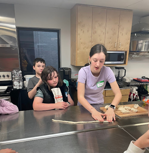 During her presentation of Germany, Lena Boas '25 demonstrates how to roll pretzels. In addition to pretzels, Boas showed other German cultural items, including lederhosen, a dirndl, and school cone.