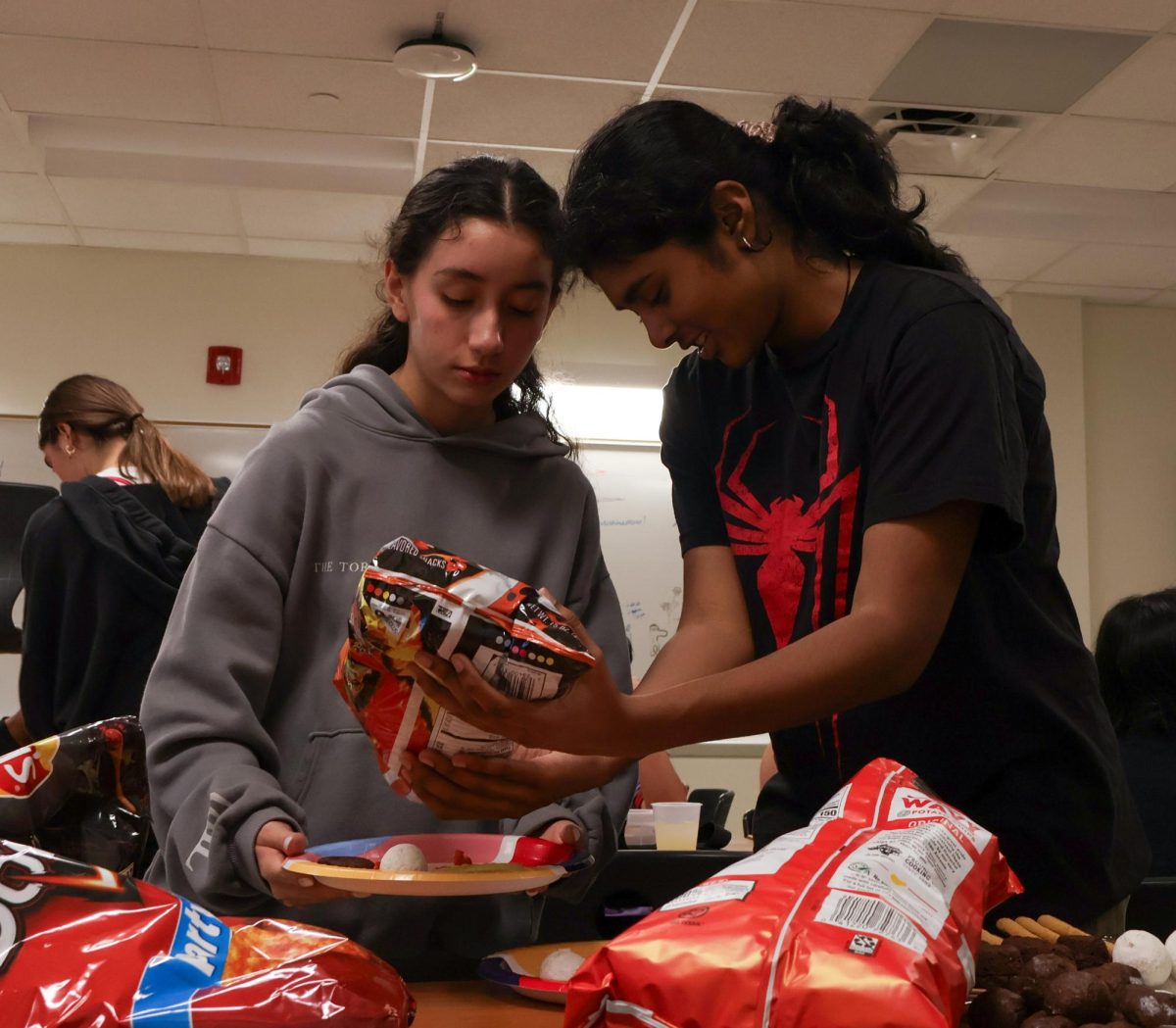 Holding her plate, Luciana Lleverino '26 steadies her food as Sahana Sakthivelmoorthy '26 helps pour cheetos into Lleverino's plate. Lleverino was elected incoming Webmaster and Sakthivelmoorthy rose to the President position. "[Bailey and Sahiti] do so much work that we don’t even know behind the scenes," Sakthivelmoorthy said. "There’s just so much work that goes into being president that I didn’t know about, so I got to learn those hacks and tricks."