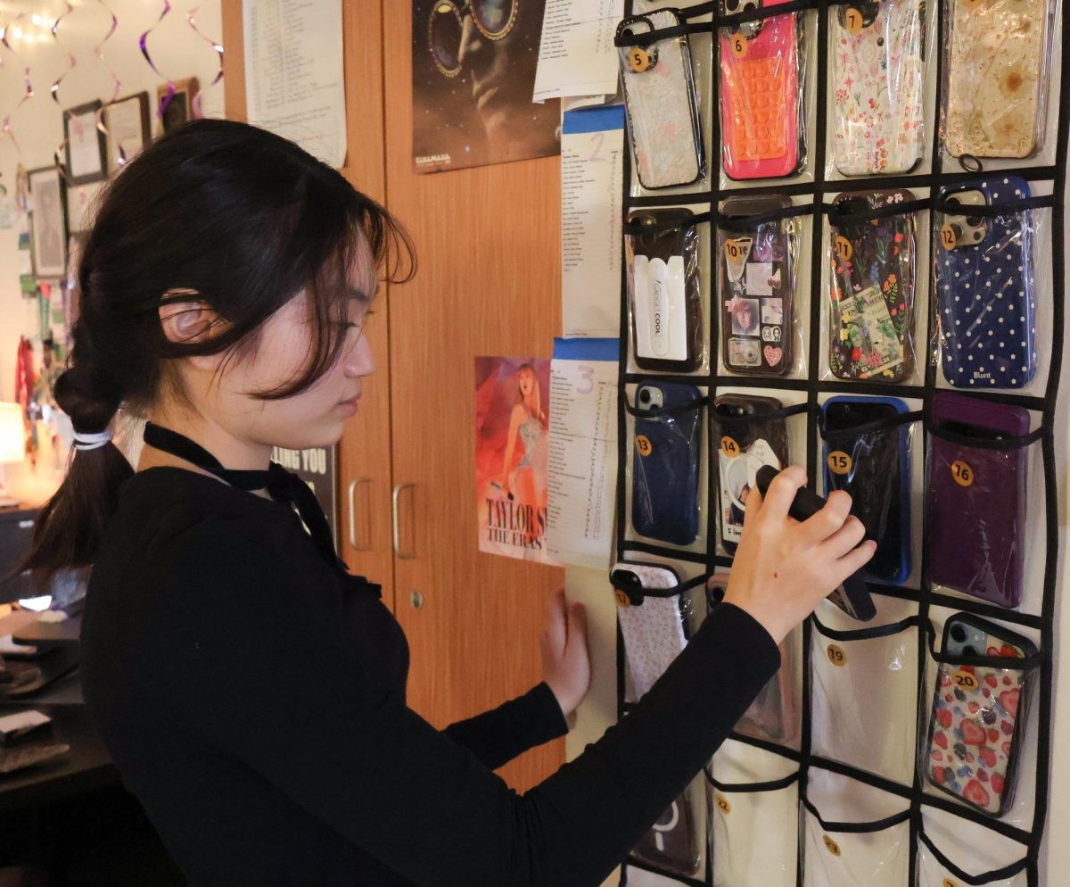 Reaching for the phone caddy, Yonnie Yang '27 places her phone into her assigned slot in her second period class. Adhering to the new student technology policy, all students across campus are required to put their phones away in caddies during class. Under House Bill 1481, personal communication devices, including phones, are prohibited during the entire school day. 
