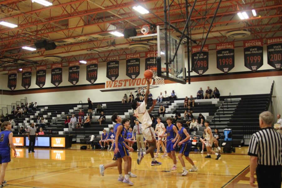 Tyson Woods '25 flies into the air with the ball inches away from the hoop. He came back down after scoring for Westwood. 